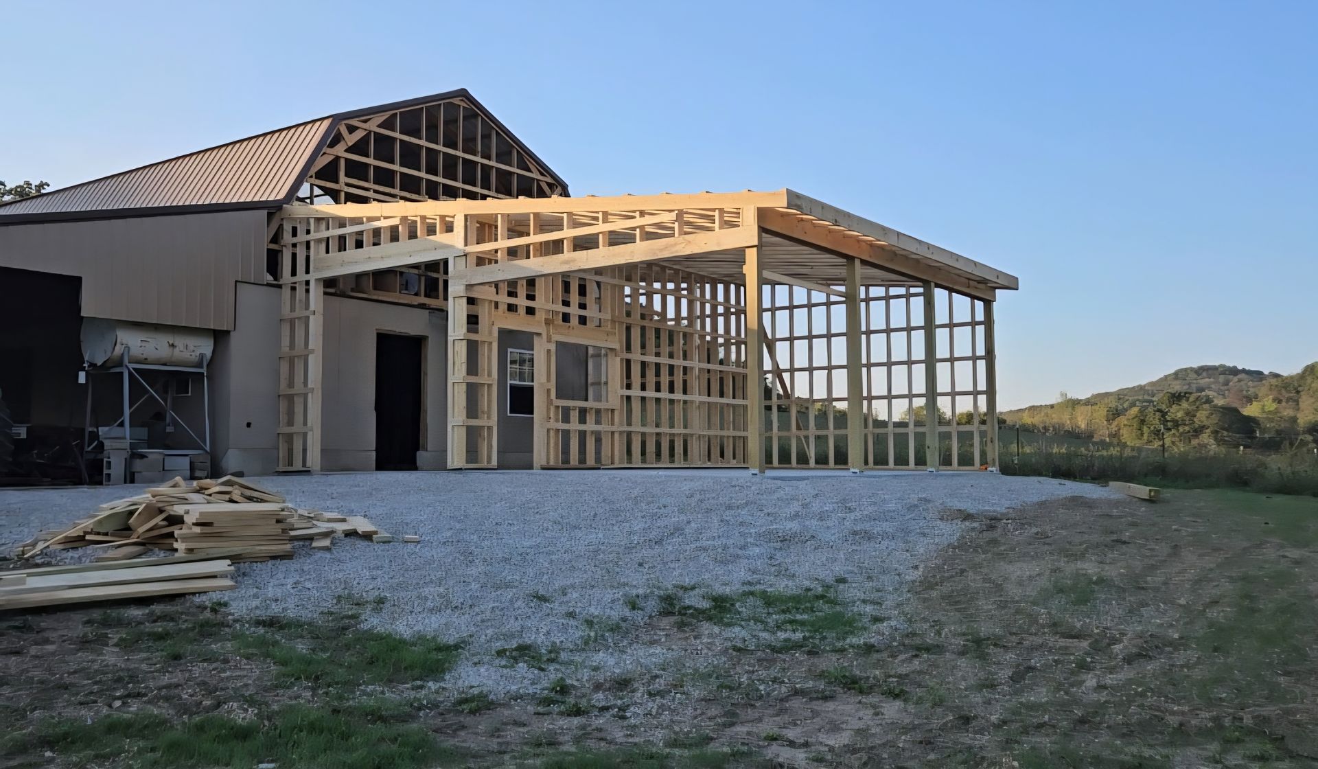 Construction of a wooden framed porch addition to a building. Gravel base, outdoors, daytime.