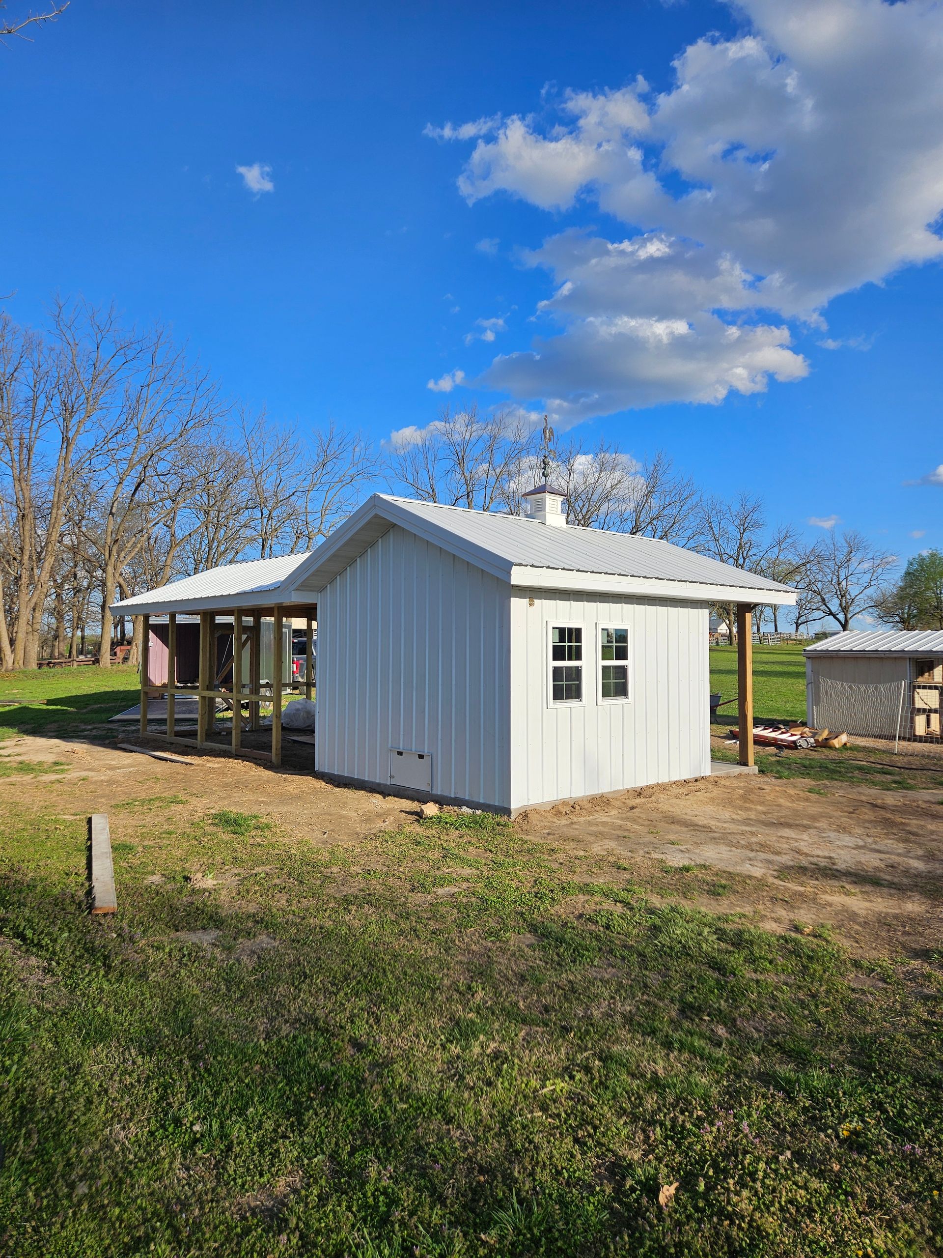 White shed and chicken coop on a grassy field, under a bright blue sky with clouds.